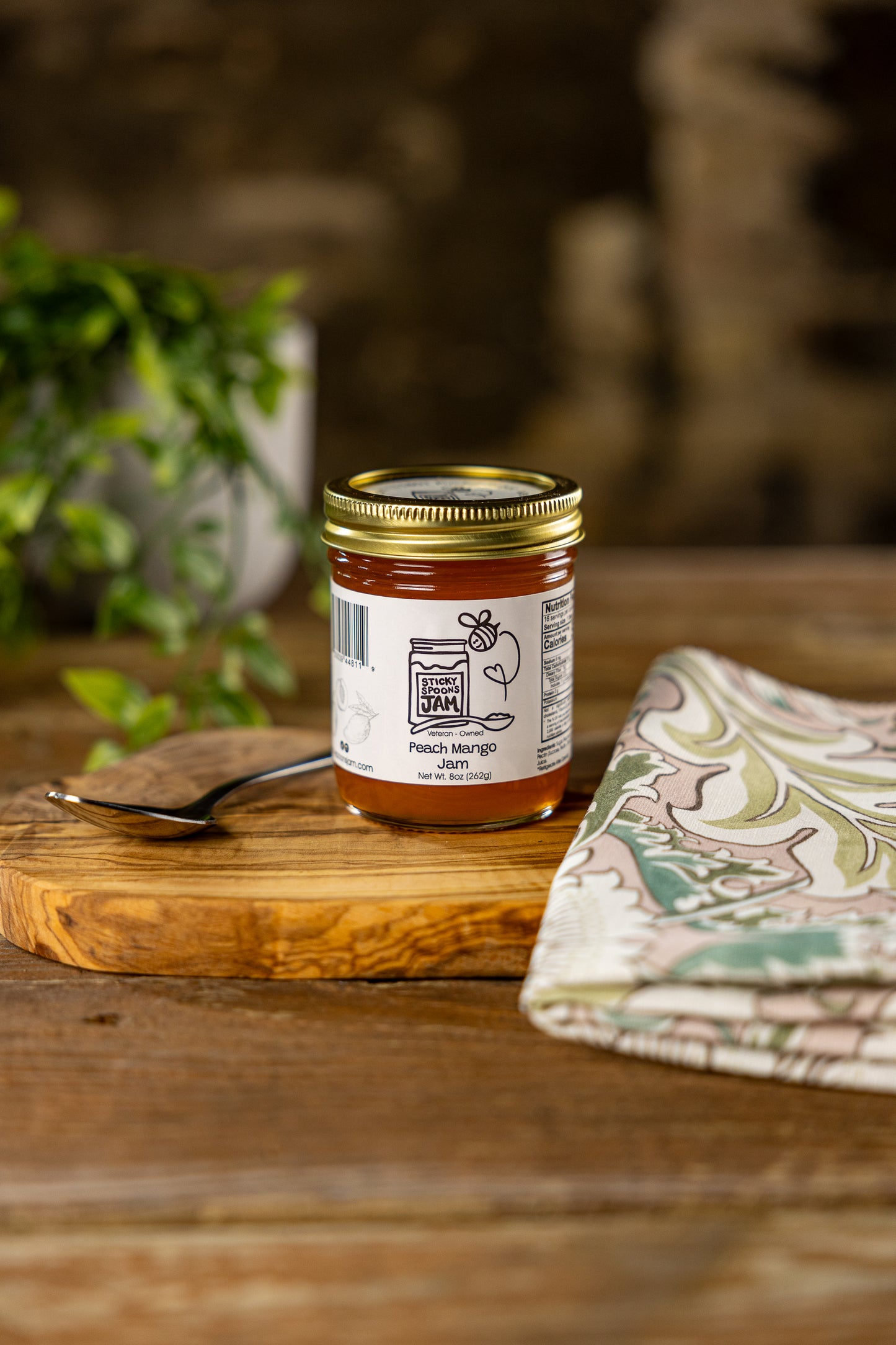 Jar of Sticky Spoons jam Peach Mango Jam on charcuterie board with spoon and napkin